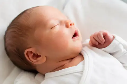 Słodki noworodek je krótko i zasypia, wtulony w białe pieluszki. Jego małe rączki są zaciśnięte w piąstki.