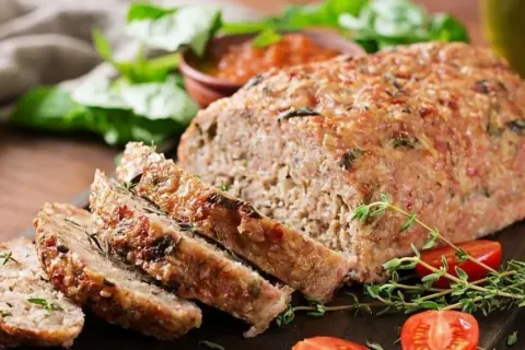 Pyszna pieczeń rzymska Ewy Wachowicz, pokrojona w plastry, podana z pomidorkami i ziołami.