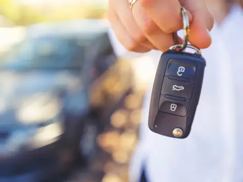 Kluczyk samochodowy z przyciskami, sugerujący jak wyłączyć immobilizer. W tle rozmyty samochód.
