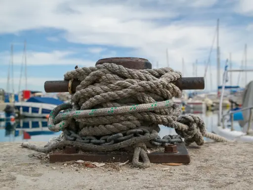 Grosse amarre enroulée sur une bitte d'amarrage, prête à supporter le poids d'un bateau. Le diamètre de la corde suggère une grande résistance.