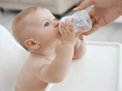 Niemowlę pije wodę z butelki. Od kiedy dziecko może pić wodę mineralną nieprzegotowaną? Od 6. miesiąca życia, gdy zaczyna rozszerzać dietę.