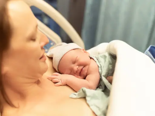 Noworodek śpi na piersi mamy, przygotowując się do karmienia. To piękny początek laktacji i więzi.
