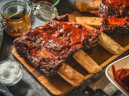 Saftige Rippchen mit BBQ-Sauce, perfekt für Ihre nächsten Grill Rezepte. Dazu grobes Salz und eine Schüssel Sauce.
