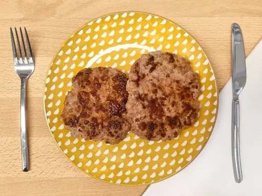 Dos hamburguesas para bebes, doradas y jugosas, servidas en un plato amarillo con puntos blancos. Cubiertos a los lados.