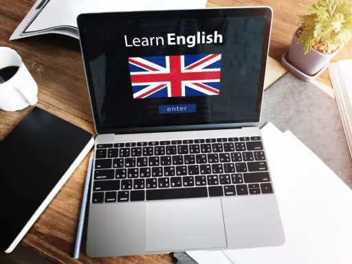 Laptop z napisem "Learn English" i flagą Wielkiej Brytanii. Obok kawa, notatnik i roślina. Idealne do nauki fce use of english.