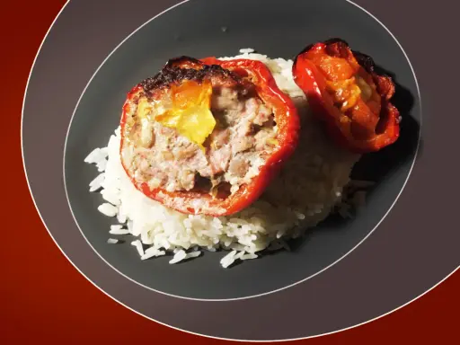 Poivrons rouges farcis à la viande, servis sur un lit de riz blanc. Une sauce légère accompagne ce plat, rappelant les saveurs des tomates farcies.