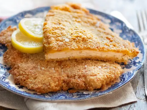 Due cotolette al forno dorate e croccanti, servite su un piatto blu e bianco con spicchi di limone.