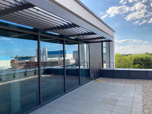 Moderne Dachterrasse mit Glasfront und Lamellendach. Ein gelber Schlauch liegt bereit, um das Flachdach anzuheben und zu pflegen.