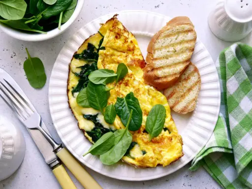 Pyszny omlet ze szpinakiem, podany z grzankami i świeżymi liśćmi szpinaku. Idealne śniadanie!