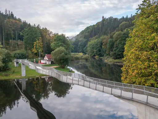 Idealna wycieczka na niedzielę na Dolny Śląsk: nowoczesny most nad spokojną rzeką, otoczony jesiennym lasem i wieżą widokową na wzgórzu.