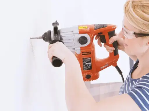 Frau bohrt mit Schlagbohrmaschine ein Loch in die Wand. Sie trägt Schutzbrille.