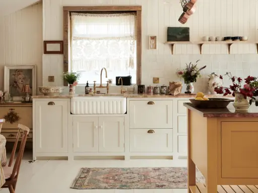Urocza kuchnia retro inspiracje: białe szafki, ceramiczny zlew, mosiężna armatura, koronkowy zazdrostka i stylowy dywanik.
