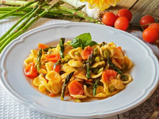 Piatto di orecchiette con asparagi freschi e pomodorini succosi, guarnito con basilico. Un classico della cucina italiana.