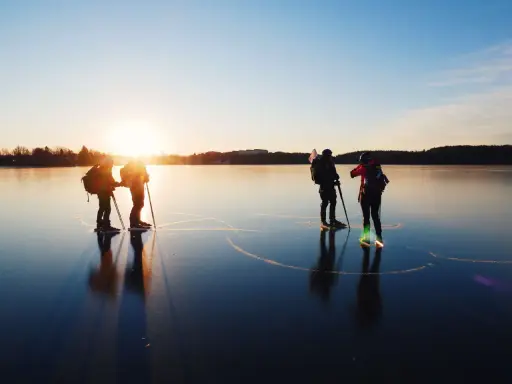 Silhuetter av skridskoåkare med stavar och ryggsäckar på en spegelblank is vid solnedgången. En magisk upplevelse av skridskoåkning i Stockholm.