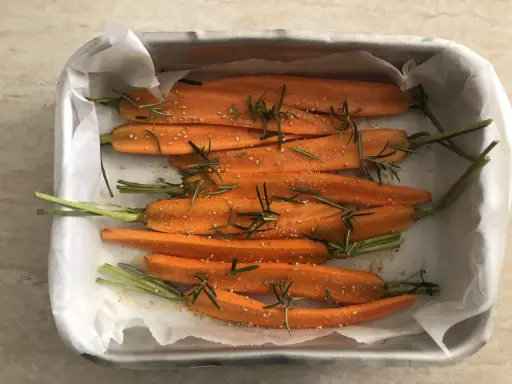Carote al forno, tagliate a metà, condite con rosmarino e semi di sesamo, pronte per essere infornate.