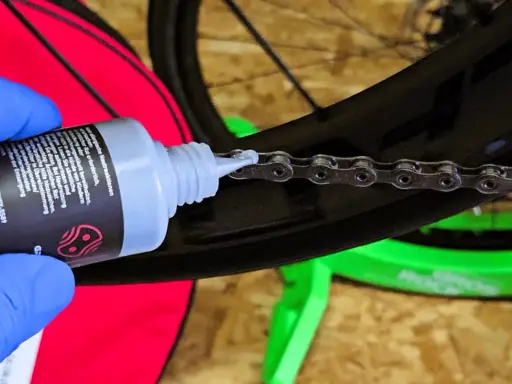 Blaue Handschuhe tragen, um die Fahrradkette wachsen zu lassen. Ein Tropfen Öl fällt auf die Kettenglieder.