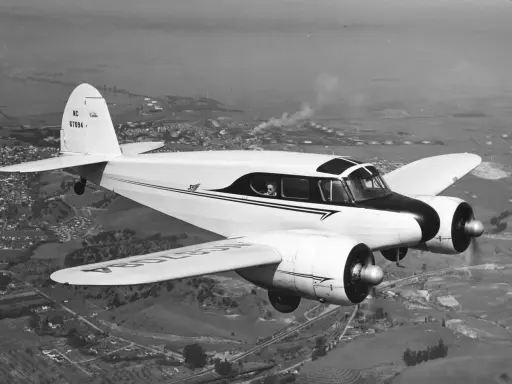 Ein weißes, zweimotoriges hochdecker flugzeug fliegt über eine Stadt und Industrieanlagen.