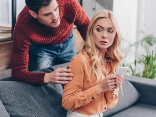Chorobliwa zazdrość mężczyzny. Patrzy na telefon partnerki, która wygląda na zaniepokojoną.