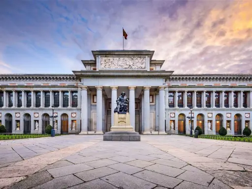 Das Prado Museum in Madrid, ein Meisterwerk der Architektur, mit einer Statue davor und einem dramatischen Himmel.
