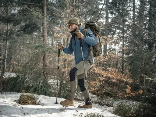 Mężczyzna w lesie z plecakiem i kijkami trekkingowymi. Prawidłowe dopasowanie kijków trekkingowych do wzrostu to klucz do komfortowej wędrówki.