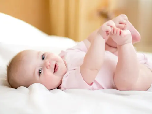 Ein lächelndes Baby von 8 Wochen liegt auf dem Rücken und spielt mit seinen Füßen.