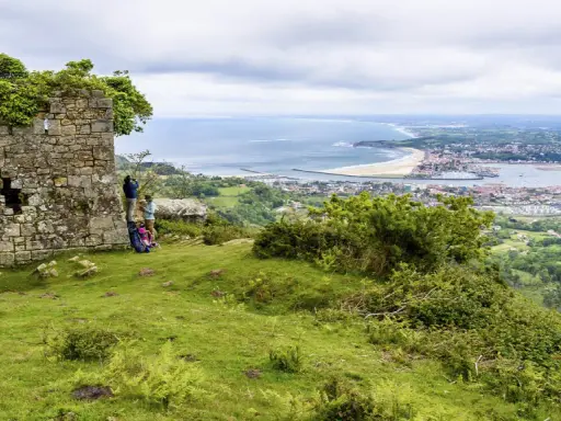 Zwei Wanderer genießen die Aussicht auf die Küstenstadt Irun, Spanien, von einer alten Ruine aus.