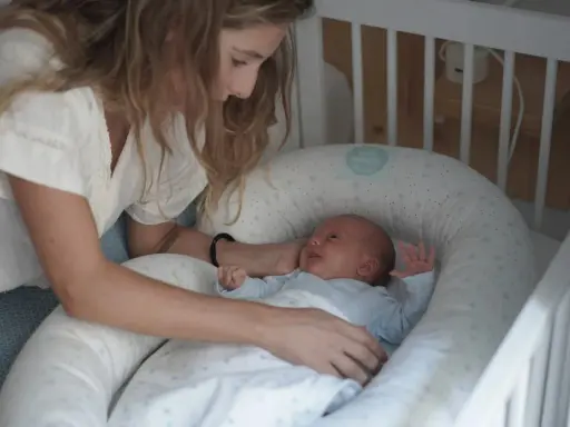 Madre observa a su bebé recién nacido, listo para sus siestas. El pequeño sonríe en su nido acogedor.