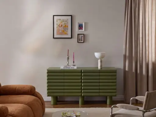 Un salotto moderno con divano color caramello, un mobile verde a coste e un gruppo di quadri appesi in modo originale.