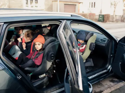 Niños en asientos de coche, uno con gorro naranja. Guía visual para como colocar silla grupo 2 3 sin isofix.