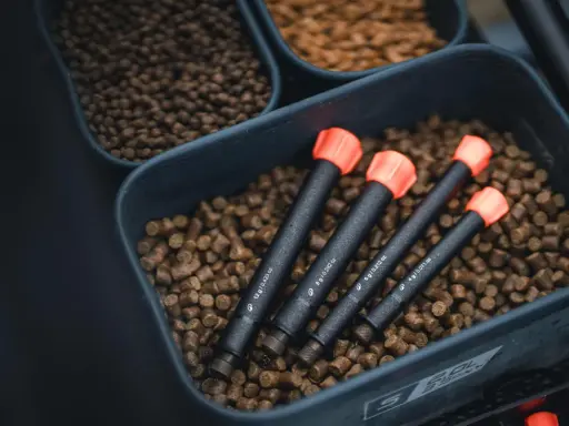Zanęta halibut na jakie ryby? W pojemniku z pelletem leżą cztery sygnalizatory brań z pomarańczowymi końcówkami.