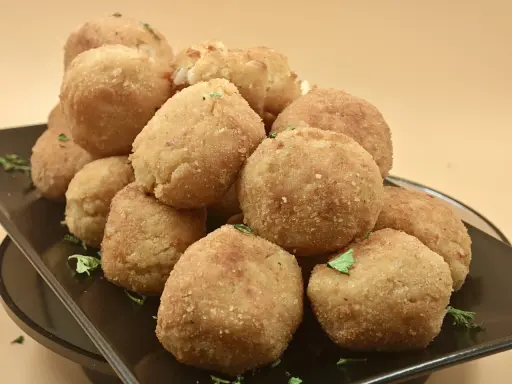 Un mucchio invitante di polpette di riso dorate e croccanti, guarnite con prezzemolo fresco, su un piatto scuro.