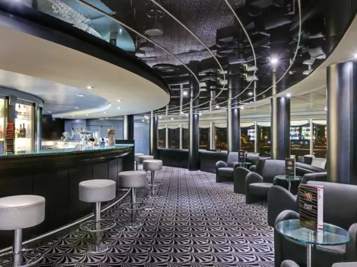 A modern bar with a curved counter, stools, lounge seating, and a patterned carpet.