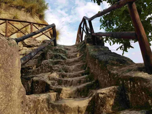 Antica scala in pietra scavata nella roccia, con ringhiera in legno, che conduce verso l'alto, evocando un'esplorazione in una grotta in Calabria.