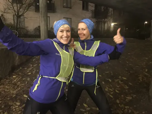 Två glada löpare i blå jackor och reflexvästar ger tummen upp, redo för ett maraton.