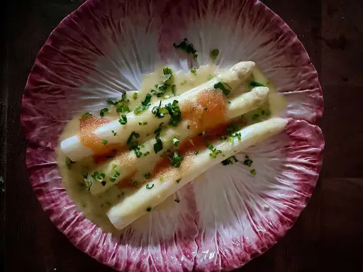 Vitt sparris med en krämig sås, toppad med kaviar och gräslök, serverad på ett rött endiveblad. En delikat ansa sparris.