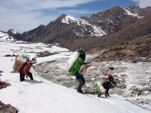 Ludzie niosący ciężkie ładunki w śniegu, zbliżając się do mount everest base camp. Góry w tle.