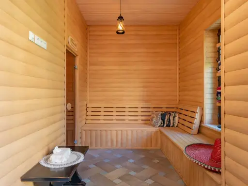 Interior de madera con bancos para relajarse, mostrando varios tipos de saunas. Un sombrero rojo y cojines decoran el espacio.