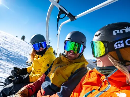 Tre vänner på väg uppför ett snöigt berg i en skidlift. Solen skiner och deras skidglasögon reflekterar den blå himlen. En perfekt resa på vintern.
