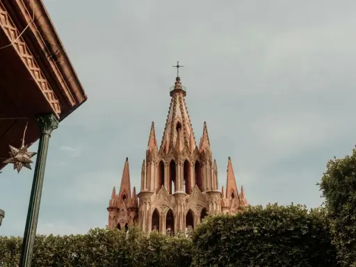 Imponująca iglica kościoła w San Miguel, otoczona zielenią, z ozdobnymi gwiazdami zwisającymi z zadaszenia.