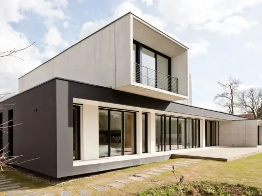 Maison moderne avec façade en béton et bardage sombre, grande baie vitrée et terrasse en bois.