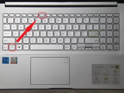 Klawiatura laptopa z podświetloną ikoną touchpada. Czerwona strzałka wskazuje klawisz Fn+Esc, który może aktywować touchpad.