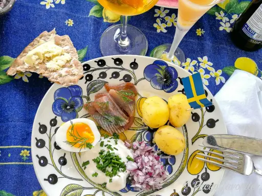 En härlig sillunch midsommar med färskpotatis, ägg, gräddfil och rödlök. En svensk flagga vajar glatt.