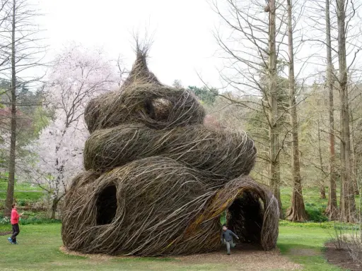Sculpture monumentale en branches tressées, ressemblant à un **arbre en cépée** géant, avec des enfants jouant autour.