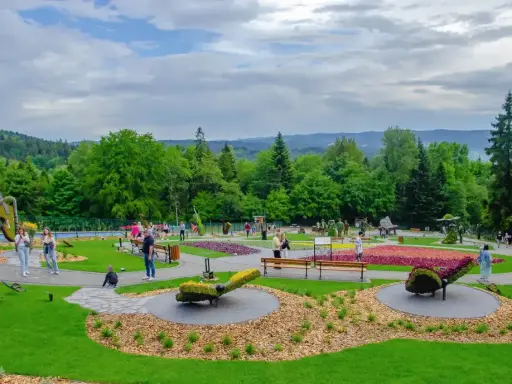 Kolorowy park z rzeźbami z kwiatów i zieleni. Widać ludzi spacerujących alejkami. Sprawdź góra parkowa cennik, by zaplanować wizytę.