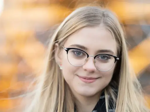 Uśmiechnięta blondynka w okularach, z rozmyciem tła. Idealna ogniskowa do portretu, podkreślająca oczy.