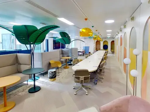 Espace de travail moderne et coloré, ce **flex office** offre des zones de réunion, des canapés confortables et des plantes décoratives pour un environnement stimulant.