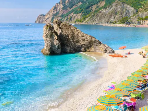 Ein malerischer italien strand mit türkisfarbenem Wasser, einem Felsen im Meer und vielen bunten Sonnenschirmen.