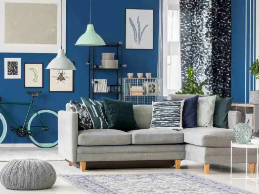 Un soggiorno moderno con divano grigio, pouf e tappeto, dominato da **colori freddi** come il blu intenso delle pareti e i toni verdi e blu degli accessori.