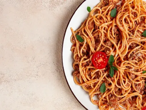 Pyszne spaghetti z mięsem mielonym, udekorowane pomidorkiem i listkami bazylii. Idealne na szybki obiad.