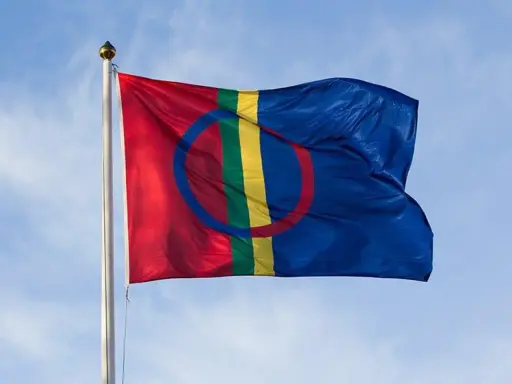 Samiska flaggan vajar stolt mot en blå himmel, en symbol för samiska nationaldagen och ett folk med djupa rötter.
